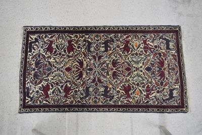 une photo d'un tapis posé sur un sol blanc, orné d'un motif noir et rouge