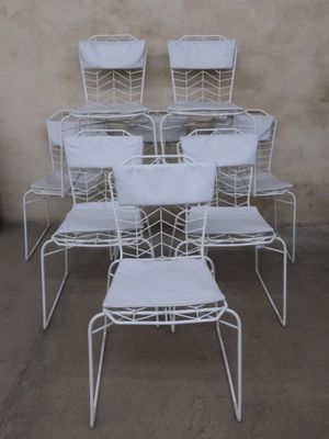 several white metal chairs are stacked on top of each other in front of a wall