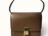 sac à main en cuir marron orné d'une boucle dorée sur fond blanc