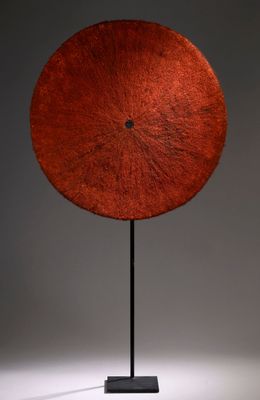 une image représentant une sculpture composée d'un disque rouge posé sur un socle noir