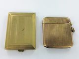 two small gold cigarette cases sitting next to each other on a white surface