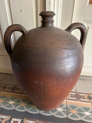 un grand vase marron posé par terre devant une porte