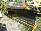 a yellow plow sitting in the grass next to a truck