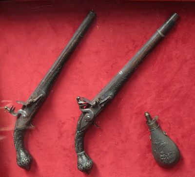 Deux vieilles armes sont exposées dans une vitrine posée sur un socle rouge