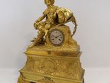 a gold clock with a statue of a man sitting on it