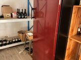 un réfrigérateur rouge au milieu d'une pièce, avec des bouteilles de vin sur les étagères