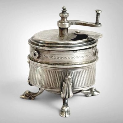 an antique silver plated coffee grinder on a stand