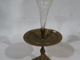 un vase en verre posé sur une plaque en laiton sur une surface blanche