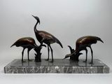 trois statues d'oiseaux en bronze posées sur un socle en marbre