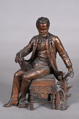statue en bronze représentant un homme assis sur une chaise avec un chien