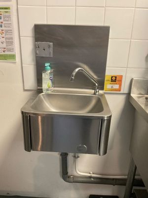 a stainless steel sink in a public restroom with a bottle of water