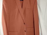 un blazer orange suspendu à un cintre sur fond blanc