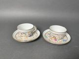 two cups and saucers with floral designs on them sitting on a table