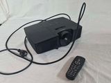 a black projector sitting on a white sheet with a remote