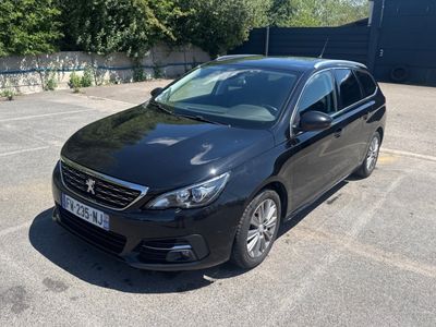 La voiture noire est garée sur le parking devant un immeuble.