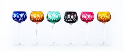 six verres à vin de couleurs différentes alignés en rang sur une surface blanche