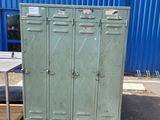 une armoire métallique verte dans un parking, à côté d'un bâtiment bleu