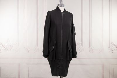 Le manteau noir est posé sur un mannequin devant un mur blanc.