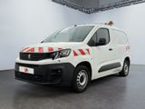 La camionnette blanche est garée dans une grande pièce ; elle porte une bande rouge et blanche sur le côté.