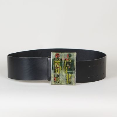 La ceinture est en cuir noir et comporte une boucle métallique sur laquelle figure l'image d'un homme vêtu de vert