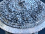 un plat ancien en argent avec un couvercle, posé sur un tissu noir