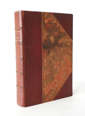 an old book with a red cover sitting on top of a white surface