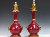 paire de vases rouges avec des bordures et des anses dorées sur un fond blanc