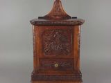 une vieille armoire en bois dont le dessus est sculpté, sur fond gris