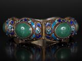 un gros plan sur un bracelet en or orné de pierres vertes et bleues
