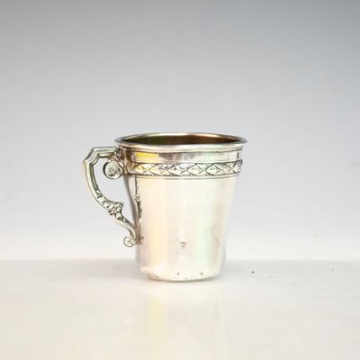 une coupe ancienne en argent munie d'une anse, posée sur un fond blanc