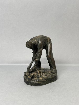 bronze statue of a man bending over to pick something off the ground