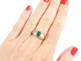 woman ' s hand with red manicured nails and a gold ring with a green stone
