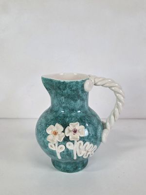 a green vase with flowers on it on a white table