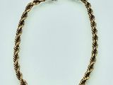 a close up of a gold rope bracelet on a white surface