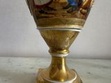 a gold vase with a painting on it sitting on a table