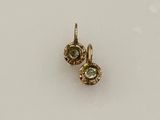 une paire de boucles d'oreilles en diamant vertes et blanches posées sur une surface blanche
