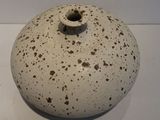 a white vase with brown spots on it on a white surface