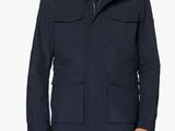 un homme vêtu d'une veste et d'un jean, debout devant un fond blanc