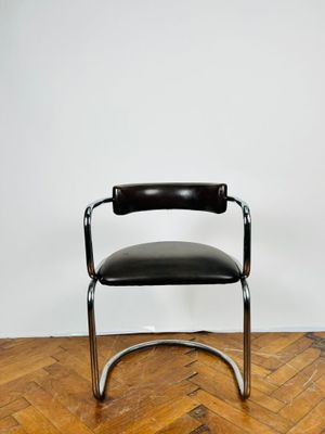 une chaise en cuir noir et chrome posée sur un parquet