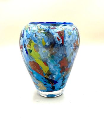 brightly colored glass vase sitting on a white surface with a light in the background
