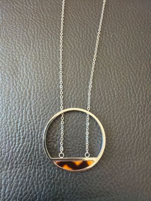 a tortoise shell and silver necklace on a black leather surface