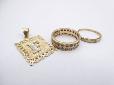 two gold rings and a gold pendant on a white surface
