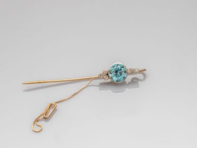 une image représentant une broche en or et en pierre bleue, accompagnée d'une chaîne