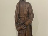 statue d'un homme assis sur une table en bois, avec un mur blanc en arrière-plan