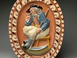 une photo d'une assiette décorative sur laquelle figure un homme assis sur un tabouret