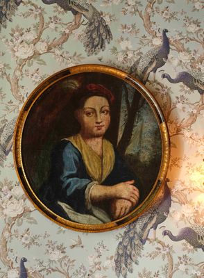 un tableau représentant une femme assise dans une pièce où l'on voit des paons accrochés au mur