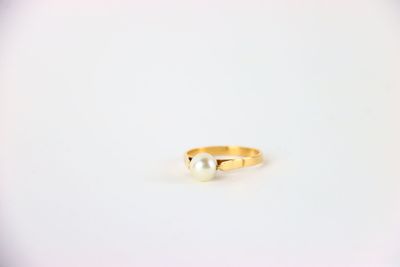 une bague en or ornée de deux perles, posée sur une surface blanche