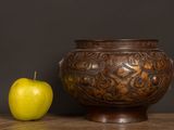 a green apple next to a brown vase on a table