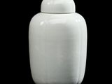 un vase blanc muni d'un couvercle, posé sur une surface noire