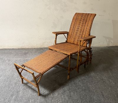une chaise longue en osier avec un repose-pieds, posée sur le sol en béton